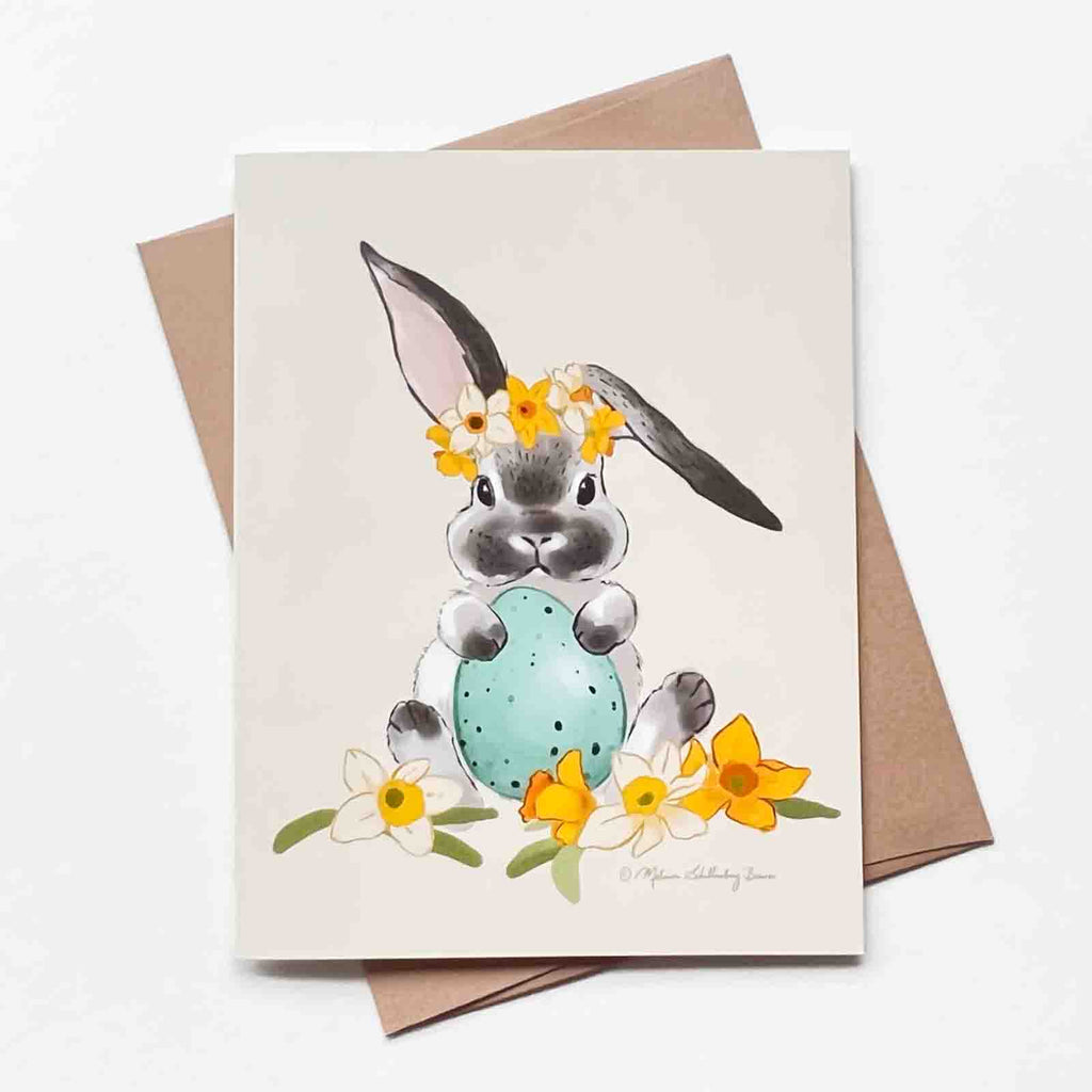 This Easter card features a gray and white bunny rabbit holding an easter egg surrounded by daffodils flowers