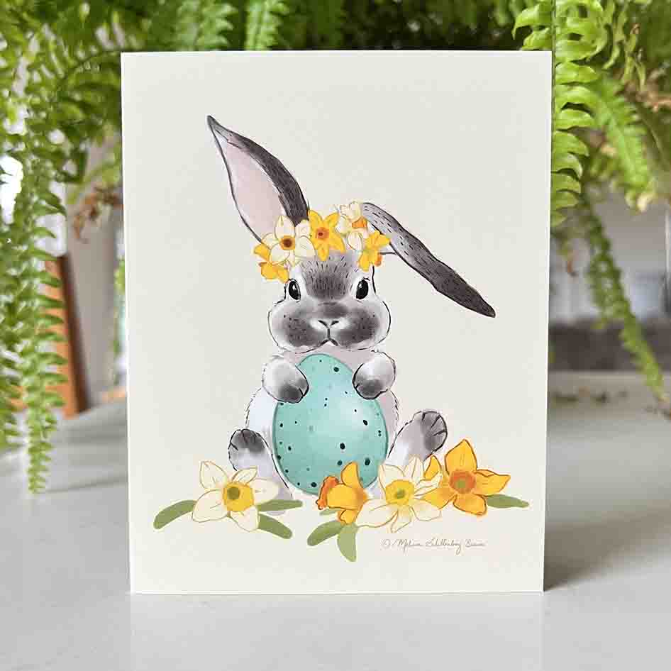 This Easter card features a gray and white bunny rabbit holding an easter egg surrounded by daffodils flowers