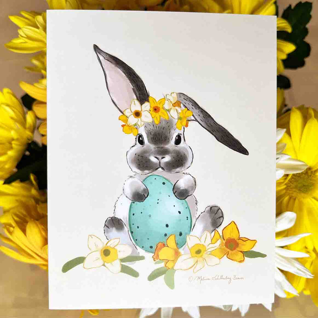 This Easter card features a gray and white bunny rabbit holding an easter egg surrounded by daffodils flowers