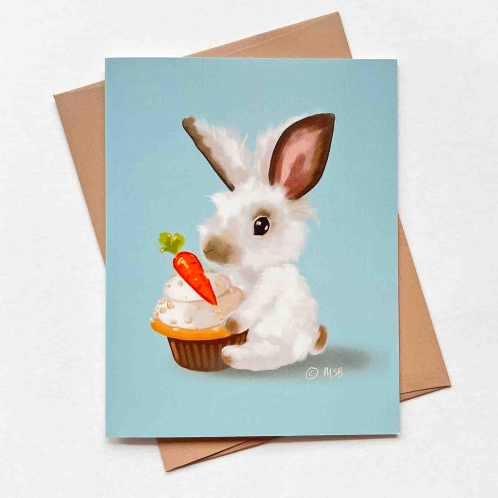 This birthday card features a cute fluffly white bunny rabbit holding a carrot cupcake against a blue backdrop