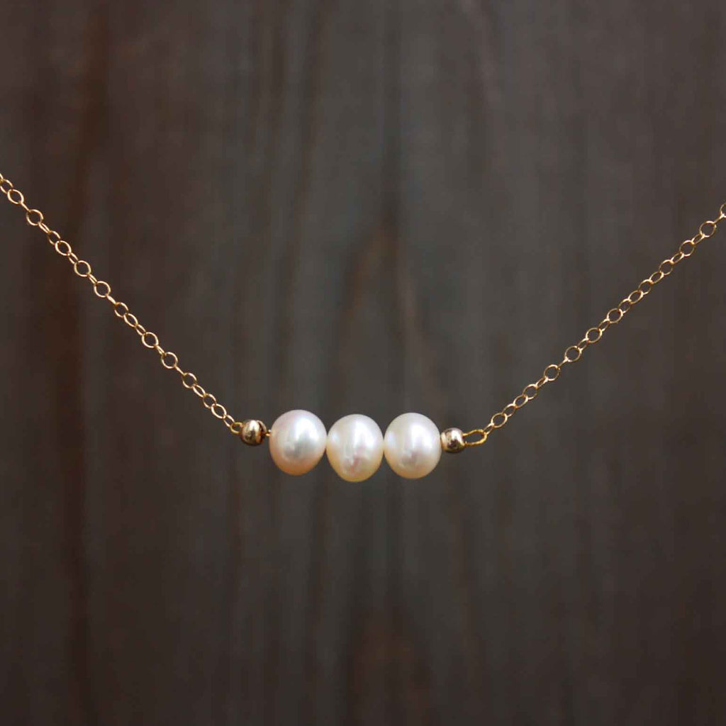 A necklace with 3 creamy coloured pearls on a dainty gold chain