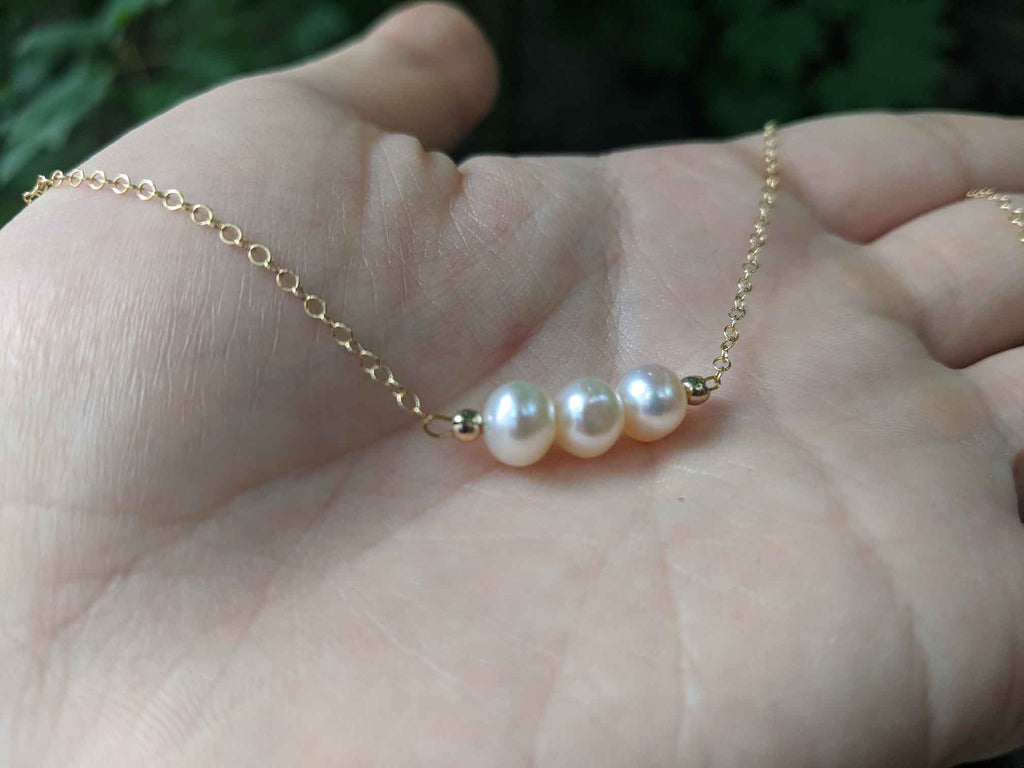 A necklace with 3 creamy coloured pearls on a dainty gold chain resting on a hand for scale